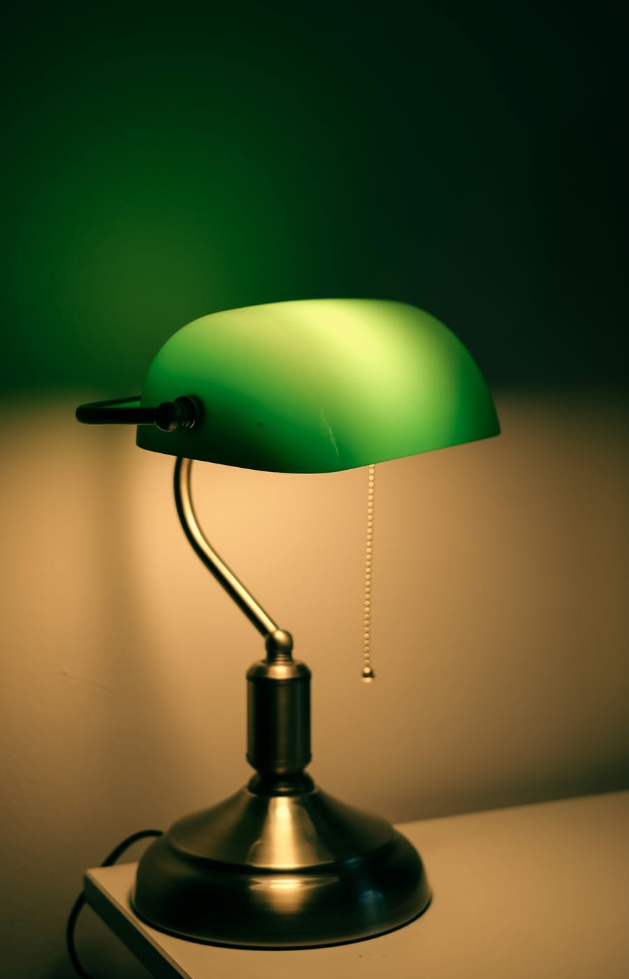 A lit bankers desk lamp with a green glass shade and brass-toned base — the photo used for this example